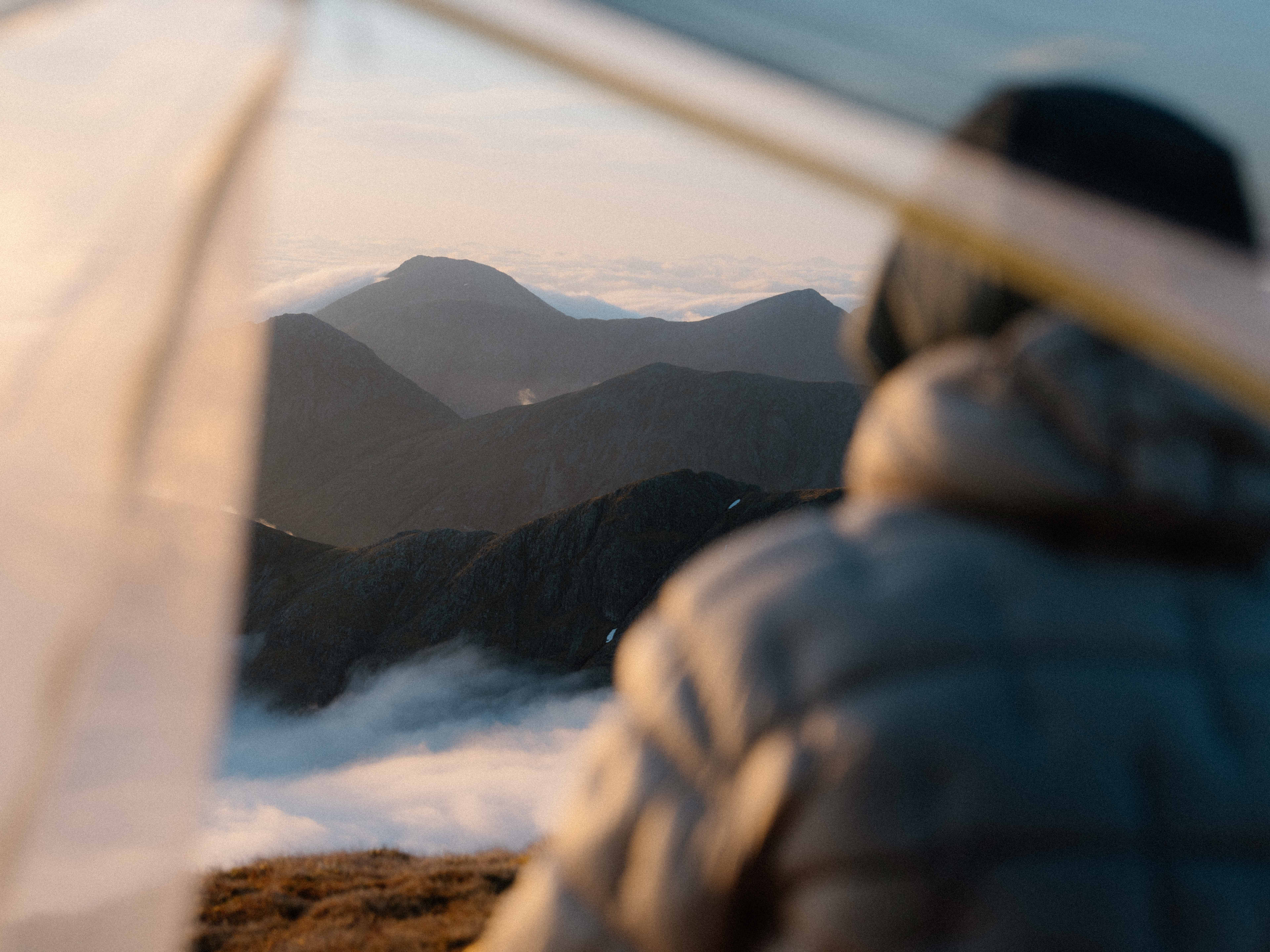 The back of a man's head as he looks out at a mountain range at sunrise. The picture is taken from inside a tent